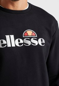 Sweat-shirt noir en coton, avec un grand logo blanc et un design coloré en forme de demi-cercle au-dessus. Col rond simple.