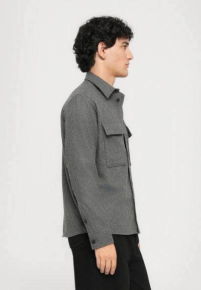Gray wool blend jacket featuring a collar, two chest pockets, button closures, and long sleeves, with a relaxed fit and subtle texture.