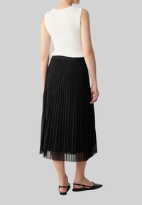 Zwarte geplooide midi-rok met een doorschijnende overlay. Gecombineerd met een aansluitend wit geribbeld mouwloos topje en zwarte slingback flats.