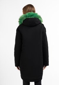 Parka nera con cappuccio e profilo in pelliccia sintetica verde, caratterizzato da una superficie liscia, maniche lunghe e un orlo curvo sul retro.