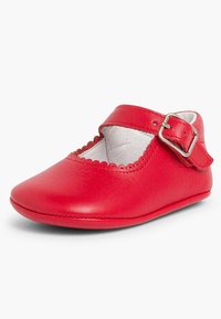 Zapato infantil rojo de cuero con punta redonda, borde festoneado y una correa con hebilla sobre el empeine. Textura suave con un forro blando.