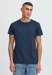 Tricou din bumbac bleumarin, cu guler rotund și mâneci scurte, având un finisaj texturat subtil și un eticheta mică în partea stângă jos.