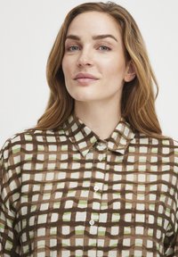 Chemise boutonnée marron et crème présentant un motif à carreaux avec des accents verts, conçue en tissu léger avec un design de col classique.