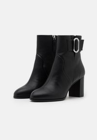 Bottes chevilles en cuir noir avec une finition texturée, un bout effilé, un talon bloc et une fermeture éclair latérale ; elles présentent un nœud décoratif et un accent de boucle argentée.