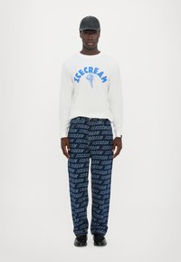 White long-sleeve shirt with blue "ICECREAM" graphic; navy pants with repeated "ICECREAM" text pattern; black cap and shoes.