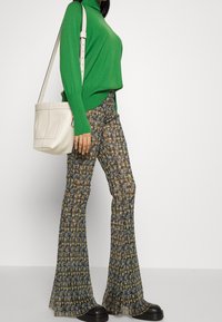 Maglione verde a collo alto abbinato a pantaloni a zampa d'elefante con motivi nei toni del blu, giallo e marrone. Modella che tiene una borsa a spalla color crema e indossa scarpe con plateau nere.