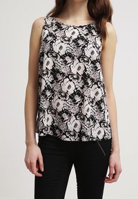 Blusa nera senza maniche con un motivo floreale bianco. Tessuto leggero, vestibilità morbida, scollatura rotonda e orlo leggermente curvo.