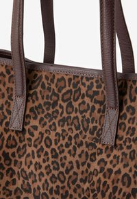 Sac fourre-tout en imprimé léopard avec des poignées en cuir marron, présentant une texture douce, une forme rectangulaire et des détails de couture contrastants.