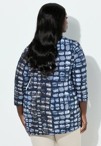 Marineblå top med et abstrakt mønster i nuancer af blå og hvid, med trekvartærmer og en afslappet pasform. Glat stoftekstur.