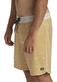 Pantaloni da bagno gialli con accenti a motivi, che presentano righe orizzontali e motivi a rombo. Vita con coulisse annodata e punti neri.