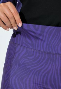 Fialové sportovní legíny mají texturovaný, vlnitý zebří vzor. Pas je hladký a pružný, což zvyšuje pohodlí a přizpůsobení.