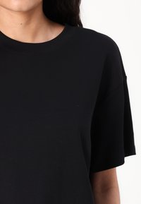 Crna majica s okruglim izrezom i kratkim rukavima. Izrađena od mekanog, teksturiranog materijala, sa opuštenim krojem i minimalnim detaljima.