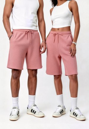 Deux personnes portant des hauts blancs, des shorts roses texturés, des chaussettes blanches et des baskets blanches avec des rayures noires, debout côte à côte.