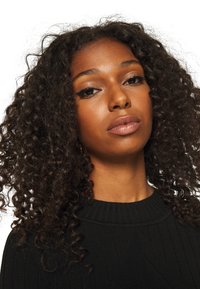 Črna rebrasta pletena jopica z okroglim izrezom. Oseba ima kodraste lase in nevtralen izraz. Ozadje je enobarvno belo.