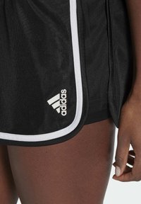 Mustat urheilushortsit valkoisilla yksityiskohdilla, joissa on teksturoitu kangas ja valkoinen Adidas-logo alareunassa.