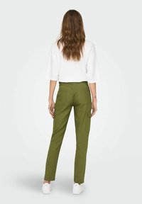 Olijfgroene cargobroek met twee achterzakken en zijcargozakken, gecombineerd met een losse witte top en witte sneakers.