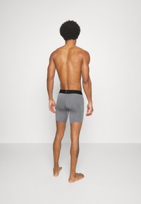 Grå boxertrosor med svart midjeband, tätt sittande design, längd till mitten av låret och slät yta, sett från baksidan.