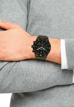 Schwarze Chronographuhr mit orangen Akzenten, strukturiertem Armband, übergroßen Ziffern auf dem Ziffernblatt, am Handgelenk getragen über einem grauen Pullover.