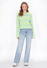 Rippstrickpullover mit grünen und blauen Streifen, langen Ärmeln und rundem Halsausschnitt. Kombiniert mit hellblauen weit geschnittenen Jeans und weißen Sneakern.