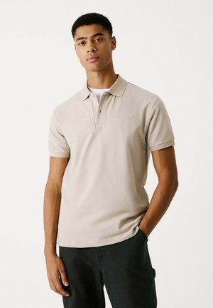 Beige kortärmad polo med klassisk krage, som har en diskret broderad logotyp på bröstet och en mjuk tygtextur.