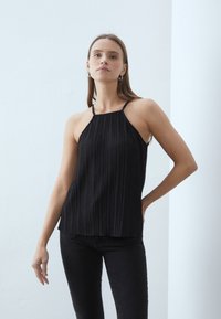 Sort, plissert halterneck topp laget av lett stoff, med tynne stropper og en avslappet passform. Båret med sorte jeans.