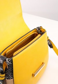 Borsa gialla in pelle con una tracolla in stampa rettile, dotata di una tasca con zip e un dettaglio in hardware dorato. Texture liscia e forma strutturata.