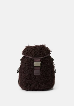 Brauner, strukturierter Stoffrucksack mit einer flauschigen Außenseite, ausgestattet mit einem oberen Deckel und einem robusten Schnallenverschluss. Mit einem Logo akzentuiert.