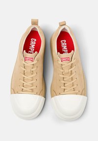 Beige leather sneakers with white rubber toe cap, round shape, and tonal laces. Red insoles feature "CAMPPER" branding. Soft texture.