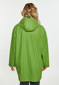 Žalias vandeniui atsparus lietpaltis su gobtuvu, pasižymintis laisvu pjaustymu ir spaudėmis rankovėse, lygia tekstūra ir ženkliniu etiketėle kaklo srityje.