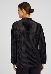 Top nero a maniche lunghe con pieghe verticali e accenti metallici. Presenta un collo arricciato e una vestibilità leggermente ampia. Tessuto liscio e strutturato.