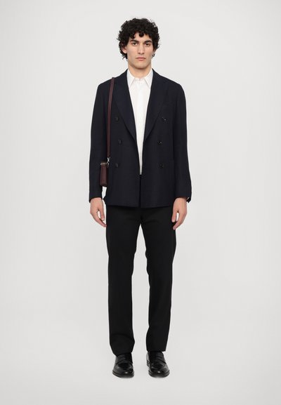 Sacou bleumarin cu dublă descheiere și butoni negri, combinat cu o cămașă albă, pantaloni negroși și pantofi negri lucioși. Geantă mică maro crossbody.