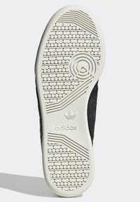 Černá podešev tenisky s texturovanou bílou gumovou vnější podrážkou, která má kruhové a horizontální drážky. Logo Adidas je vyraženo blízko paty.