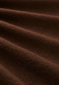 Tissu marron avec une surface douce et texturée, présentant des vagues et des plis subtils, caractéristique d'un matériau pelucheux idéal pour les vêtements ou le rembourrage.