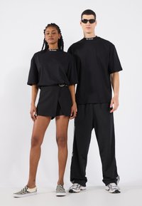 Sort oversized t-shirts, sorte shorts med bælte og sorte træningsbukser. Bemærkelsesværdige accessories inkluderer ternede slip-on sko og solbriller.