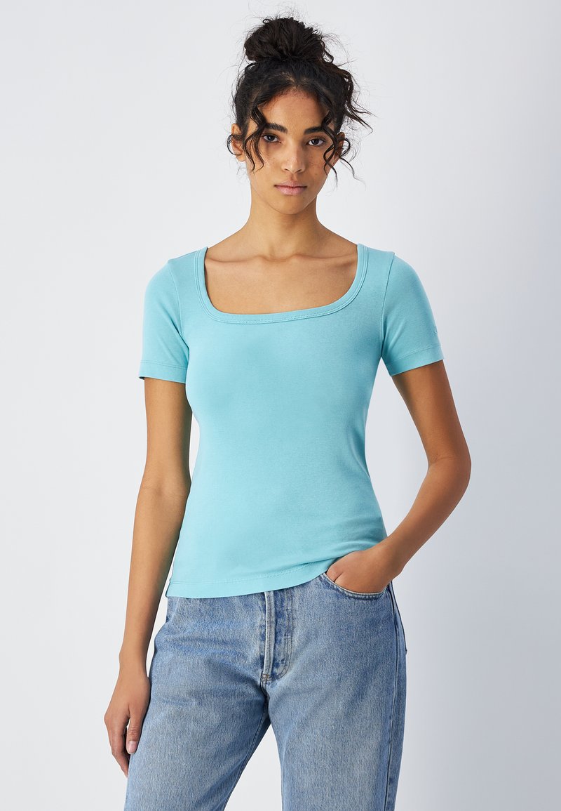 Jasnoniebieska koszulka z krótkim rękawem, z kwadratowym dekoltem, dopasowana, wykonana z miękkiego materiału, zestawiona z wysokimi, jasnodżinsowymi spodniami.