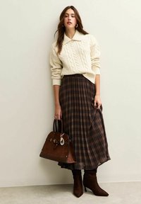 Cremfarbener Strickpullover mit Kabelmuster, brachter karierter Maxirock, braune Wildlederhandtasche und knielange, braune Stiefel mit Absatz. Minimalistisches Design und neutrale Farben.