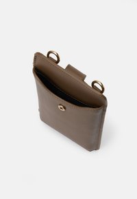 Geantă din piele maro, având un buzunar frontal cu o închidere din metal auriu și două inele rotunde pe laterale. Textură netedă.