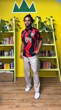 Camisa de manga corta para hombre con un diseño ondulado en negro y rojo, que presenta el número "04". Combinada con pantalones beige y zapatillas blancas.