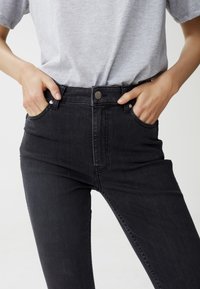 Höga svarta denimjeans med en slät textur, framfickor och stängning med metallknapp. Fitted design med minimalt med detaljer.
