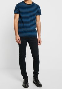 Camiseta de manga corta a rayas azules y negras con cuello redondo, combinada con pantalones negros ajustados y zapatos negros.