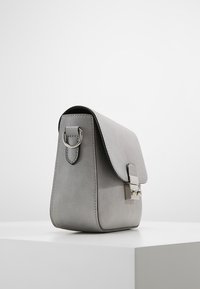 Šedá kožená kabelka s hladkou texturou, obdélníkovým tvarem, zaoblenými okraji, klopovým uzávěrem a stříbrným kovovým detailem spona.