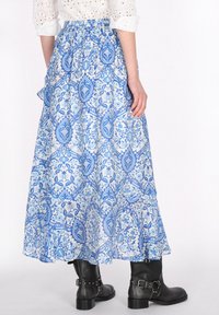 Maxi sukně v modro-bílém květinovém vzoru, vyrobená z lehké tkaniny. Má elastický pas a rozšířený design. Viditelné černé kotníkové boty.