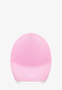 Silicone ansiktsrensingsenhet i rund form, med fine bust i lys rosa. Gjennomsiktig base og merkevarenavn "FOREO" synlig.