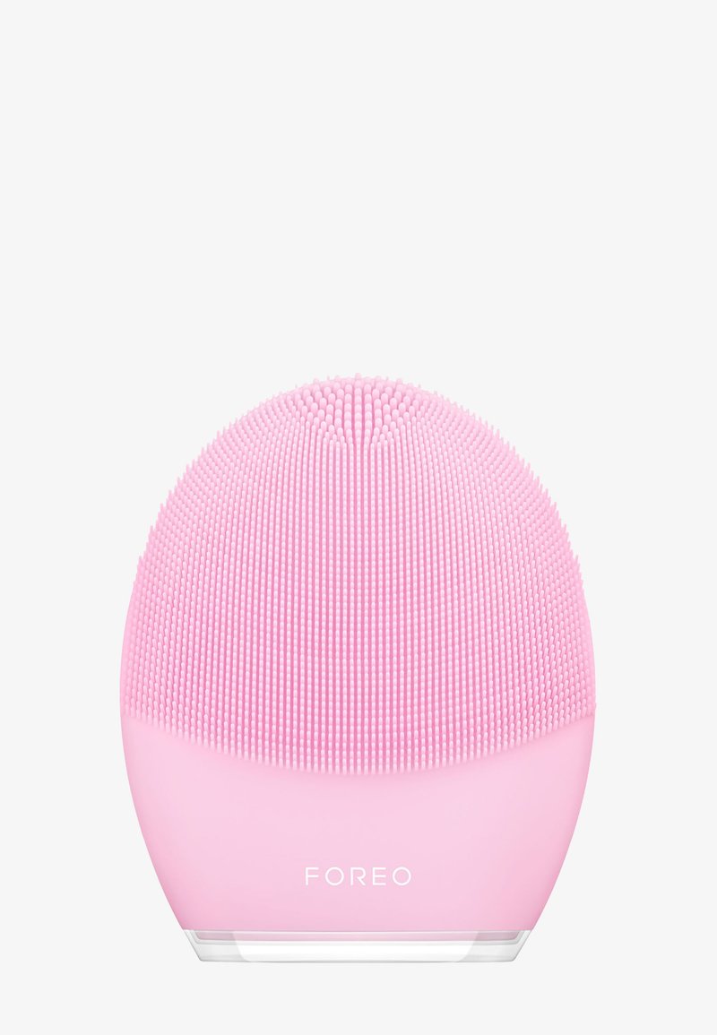 Silicone ansiktsrensingsenhet i rund form, med fine bust i lys rosa. Gjennomsiktig base og merkevarenavn "FOREO" synlig.