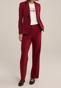 Bordeaux skräddarsydd kavaj och matchande byxor, med en mjuk textur, enknappslåsning och snedställda fickor. Vit grafisk t-shirt under.