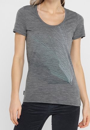 Femme portant un t-shirt gris à manches courtes avec un motif abstrait de lignes bleu clair et blanc à l’avant.