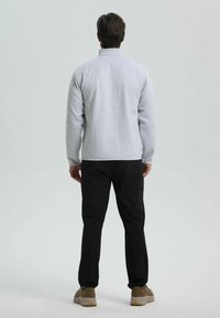 Svetle šedá fleecová bunda s vysokým límcem, spárovaná s černými kalhotami a hnědými botami. Hladká textura a volný střih.