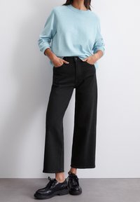 Vaaleansininen neule, jossa on ribattu kaula-aukko, yhdistettynä korkeavyötäröisiin mustiin leveälahkeisiin farkkuihin ja mustiin nauhakenkiin. Rentoa ja mukavaa asua.