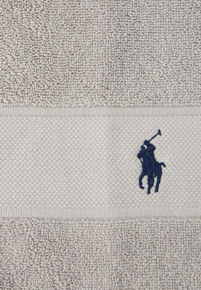 Πετσέτα ανοιχτό γκρι με υφή, με οριζόντια ταινία που φέρει ένα λογότυπο παίκτη πόλο κεντημένο σε σκούρο μπλε χρώμα.