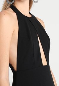 Svart halterklänning med djup urringning, sömlös design och spetsdetaljer på sidan. Tyget ser slätt och åtsittande ut.